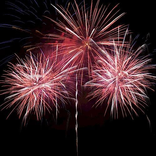 Colorful red, blue, and white fireworks burst in a dark night sky, forming multiple starburst trails.