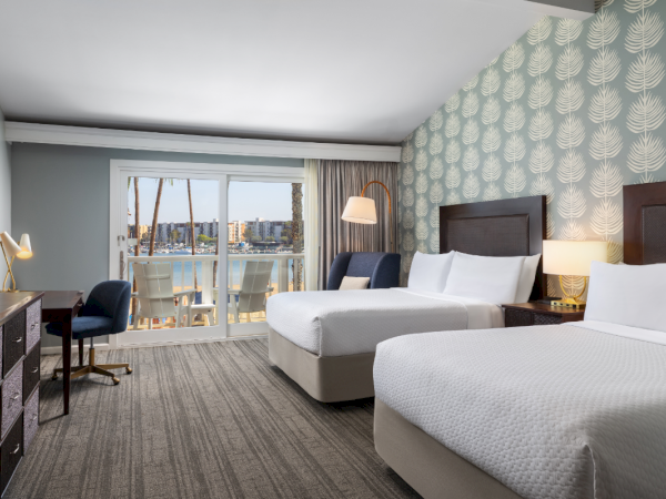 A modern hotel room with two queen beds, a desk, a chair, patterned wallpaper, and a balcony with a city view. Top it at 140 characters, always ending the sentence.