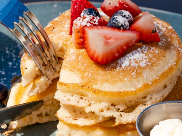 A stack of pancakes topped with strawberries and blueberries, accompanied by a small container of cream on a plate.