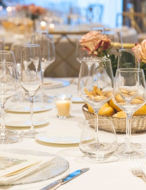 A formal dining table set for a banquet with multiple glasses, plates, silverware, candles, and a floral centerpiece, ready for guests.