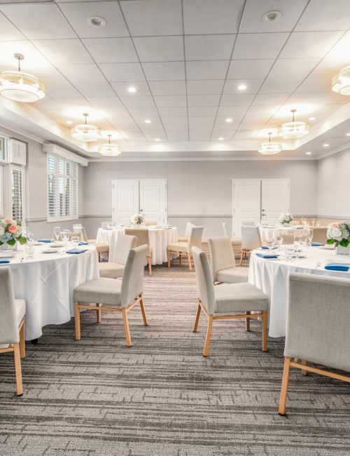 Elegant banquet room set for a meal: round tables with white linens, comfy gray chairs, soft lighting, and a neutral, airy vibe.