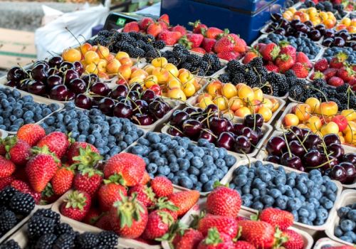 A colorful fruit market with strawberries, blueberries, cherries, blackberries, and peaches arranged in trays at a stall. Ending the sentence.