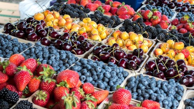 A colorful fruit market with strawberries, blueberries, cherries, blackberries, and peaches arranged in trays at a stall. Ending the sentence.