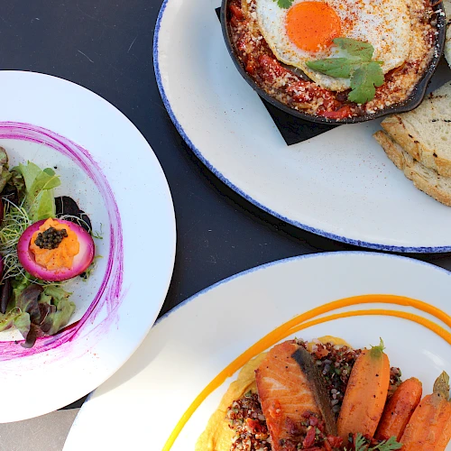 A colorful assortment of dishes: a greens salad with pink dressing and peach slices, a plate with toasted bread, and a plate with roasted carrots and meat, all plated beautifully.