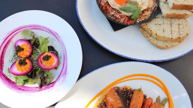 A colorful assortment of dishes: a greens salad with pink dressing and peach slices, a plate with toasted bread, and a plate with roasted carrots and meat, all plated beautifully.