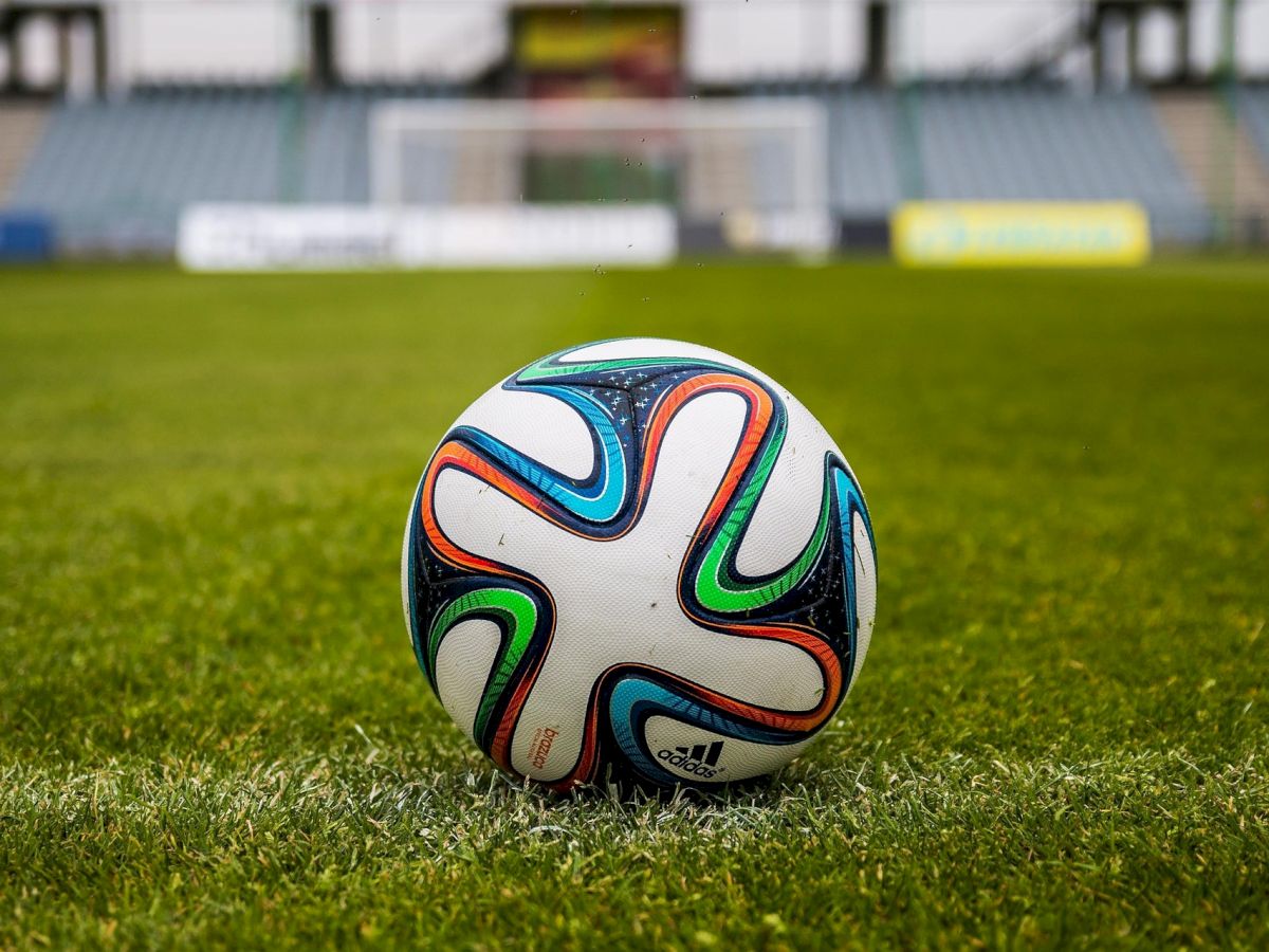 A colorful soccer ball on a grassy field, with a stadium backdrop in the distance, ready for play.